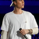 Justin Bieber performing in a white shirt and black cap in 2015