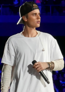 Justin Bieber performing in a white shirt and black cap in 2015